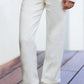 A junior girl wearing Tartine et Chocolat’s Girls' Drawstring Bow Trousers stands on a wooden floor, paired with a cream knit sweater and blue-and-white sneakers.