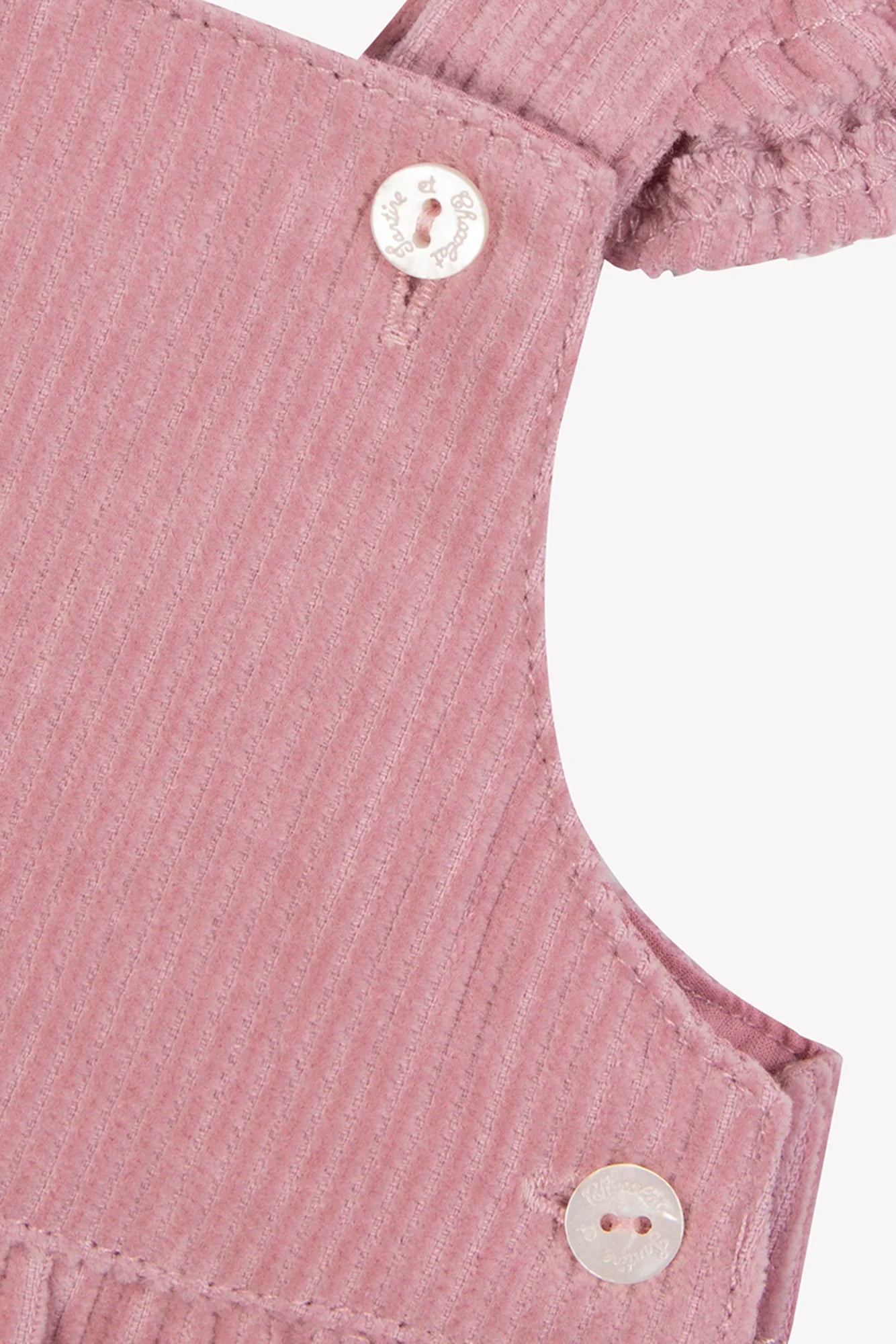 Close-up of Tartine et Chocolat Baby Girl's Velvet Overalls, designed in eglantine pink with delicate ruffles and two white buttons on the shoulder straps.