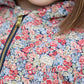 Close-up of a child in the Tartine et Chocolat Girls' Liberty Fabric Down Jacket, featuring a vibrant floral pattern and gold zipper, with brown hair partially visible.