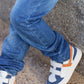 A child in Tartine et Chocolat Baby Boys' and Boys' Cotton Jeans sits cross-legged on a stone surface, wearing blue jeans and white sneakers with orange accents.