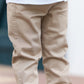 A boy from the baby and junior range stands indoors wearing Tartine et Chocolat Baby Boys' and Boys' Trouser Pants, a white ribbed shirt, and tan sneakers with white laces.