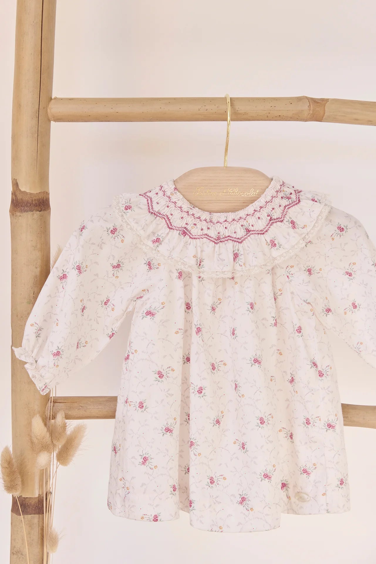 The Tartine et Chocolat Baby Girls' Ruffle Collar Embrodery Floral Dress, featuring delicate embroidery and long sleeves, is displayed on a wooden hanger against a bamboo rack.