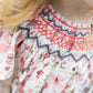 Close-up of a child in a Tartine et Chocolat Baby Girls' and Girls' Smocked Collar Floral Dress, showing detailed smocking with red and blue embroidery on the collar; part of her blonde hair is also visible.