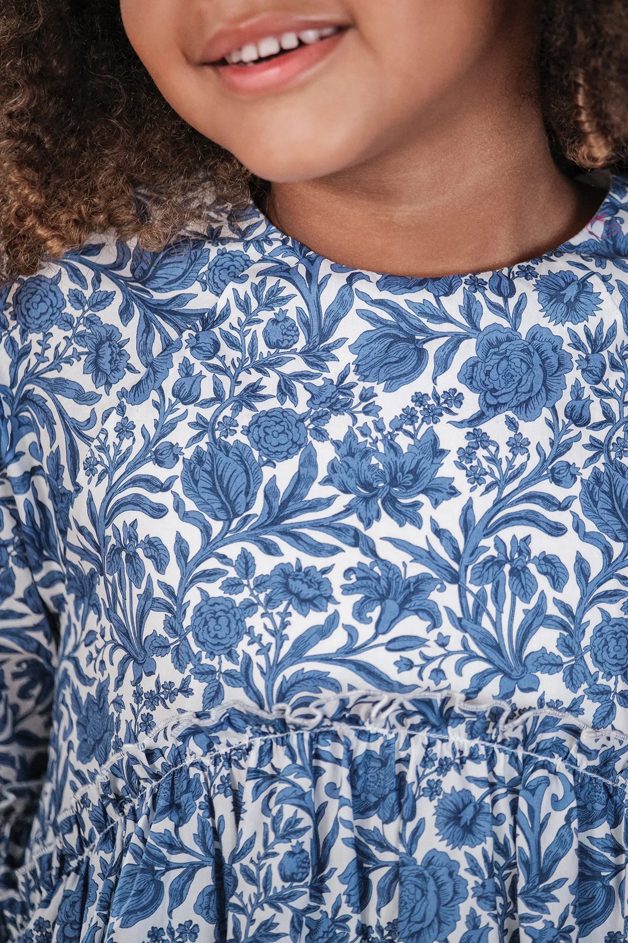 A girl wears the Tartine et Chocolat Girls' Liberty Printed Dress in blue and white, smiling with only the lower half of her face visible.
