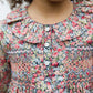 A girl models the Tartine et Chocolat Girls' Liberty Smocked Ruffle Sleeved Floral Dress, featuring decorative buttons and a charming floral print—elegantly shown from shoulders to chin.