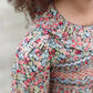 A close-up of a child in the Tartine et Chocolat Girls' Liberty Smocked Ruffle Sleeved Floral Dress, featuring charming floral patterns and delicate ruffled sleeves.