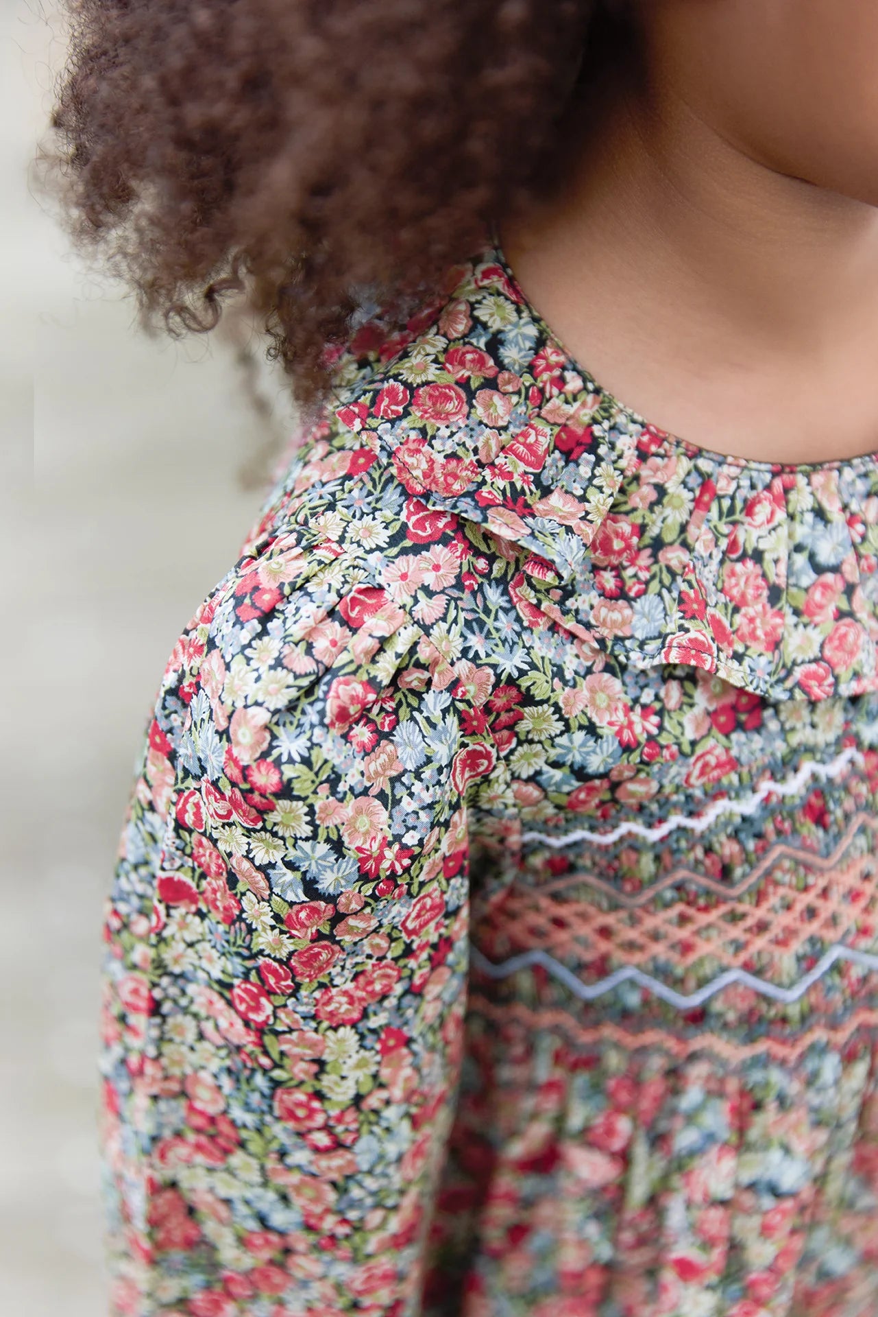 A close-up of a child in the Tartine et Chocolat Girls' Liberty Smocked Ruffle Sleeved Floral Dress, featuring charming floral patterns and delicate ruffled sleeves.