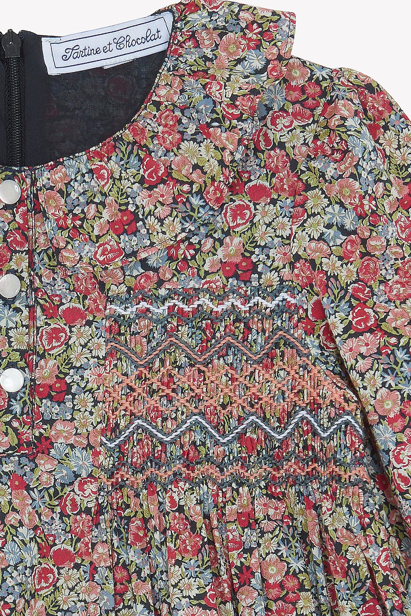 Close-up of Tartine et Chocolat’s Girls' Liberty Smocked Ruffle Sleeved Floral Dress, featuring smocking, silver buttons, and a visible brand label at the ruffled collar.