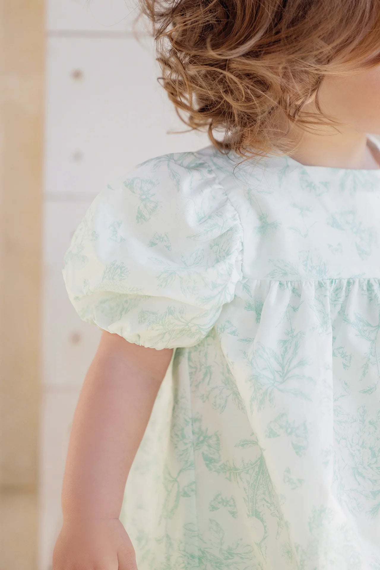 A young child is shown from the shoulders down, wearing the Tartine et Chocolat Baby Girls' and Girls' Puff Sleeve Dress with a subtle floral pattern; part of her face is out of frame.