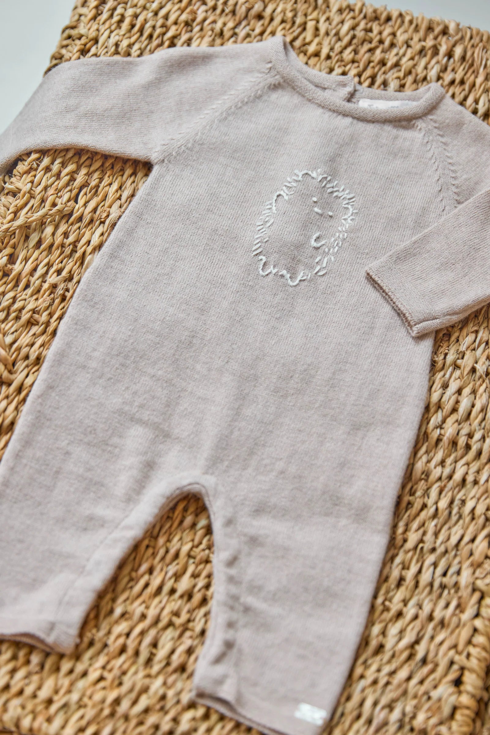 The Tartine et Chocolat Baby Boys' Embrodery Hedgehog Long Sleeved Jumpsuit in beige features a handmade hedgehog embroidery on the chest and is displayed on a woven mat.