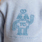 A boy wears the Tartine et Chocolat Baby Boys' and Boys' Jogger Outfit—a blue-grey sweatshirt with an embroidered robot and "TC" lettering—perfect for a stylish, comfy look.