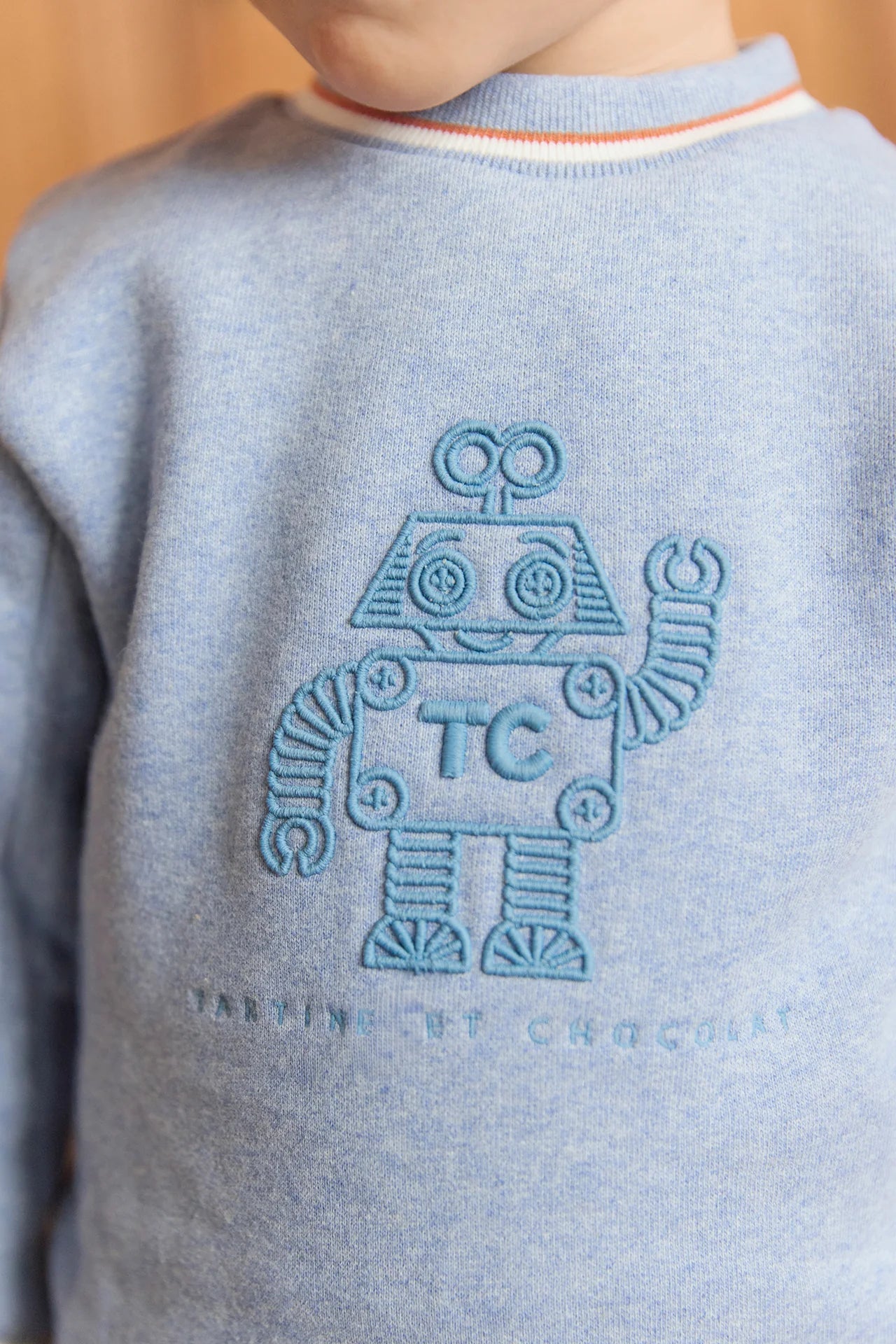 A boy wears the Tartine et Chocolat Baby Boys' and Boys' Jogger Outfit—a blue-grey sweatshirt with an embroidered robot and "TC" lettering—perfect for a stylish, comfy look.