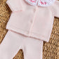 The Tartine et Chocolat Baby Girls' Ruffle Collar Long Sleeved Outfit in light pink wool and cashmere features a buttoned cardigan, pants, and a white collar with red embroidery, shown here on a woven surface.