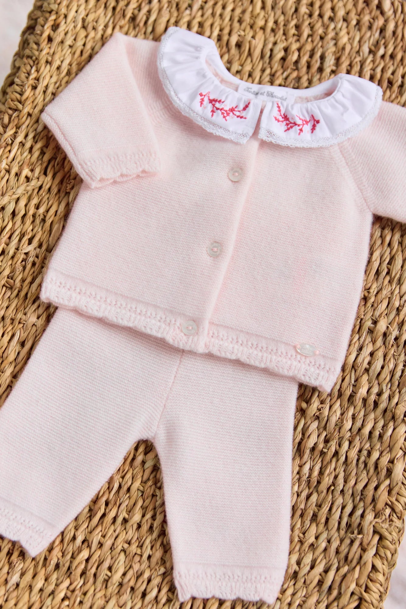 The Tartine et Chocolat Baby Girls' Ruffle Collar Long Sleeved Outfit in light pink wool and cashmere features a buttoned cardigan, pants, and a white collar with red embroidery, shown here on a woven surface.