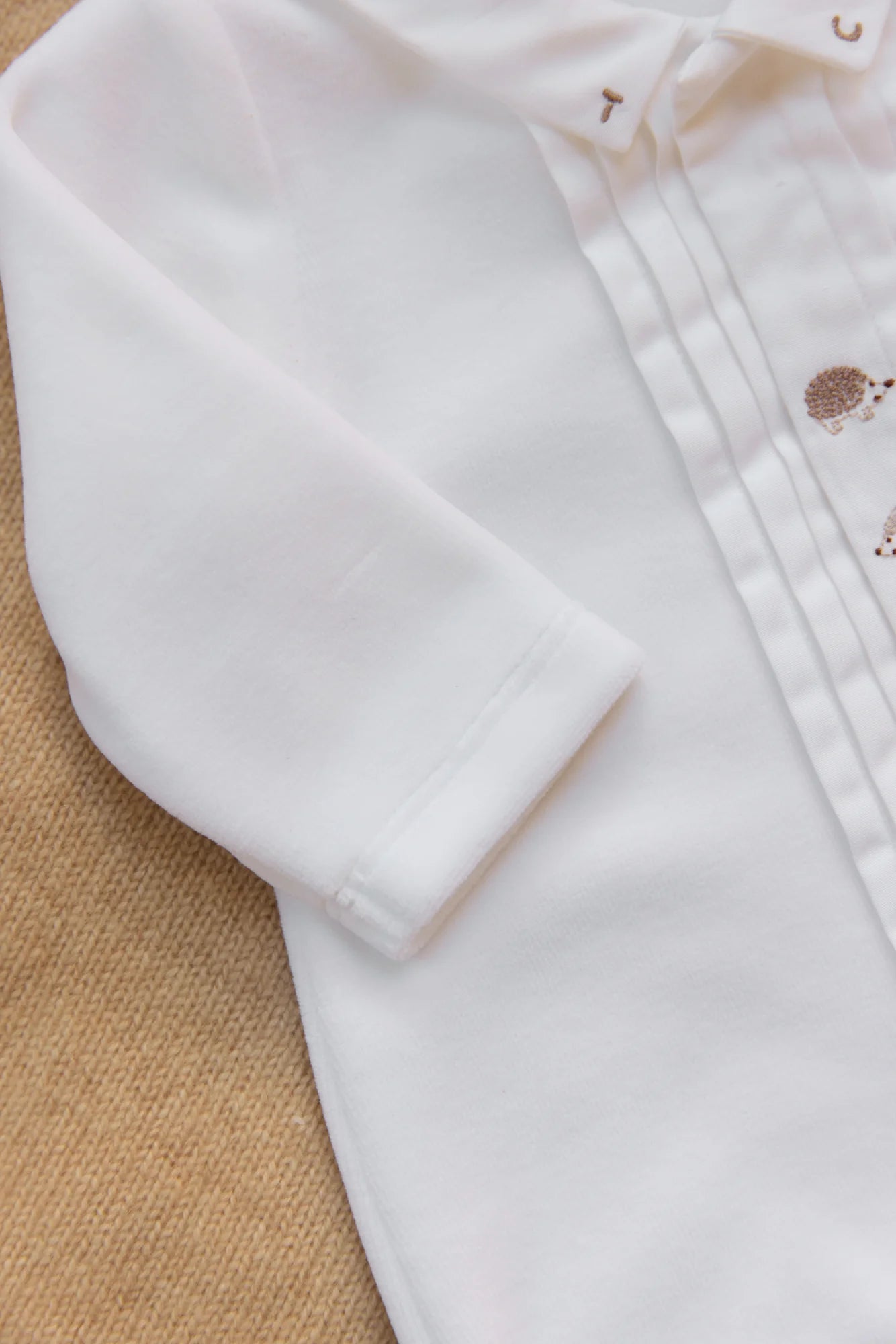 Close-up of Tartine et Chocolat Baby Boys' Hedgehog Pajamas with stitched details and cute embroidered hedgehogs, displayed on a textured beige background.