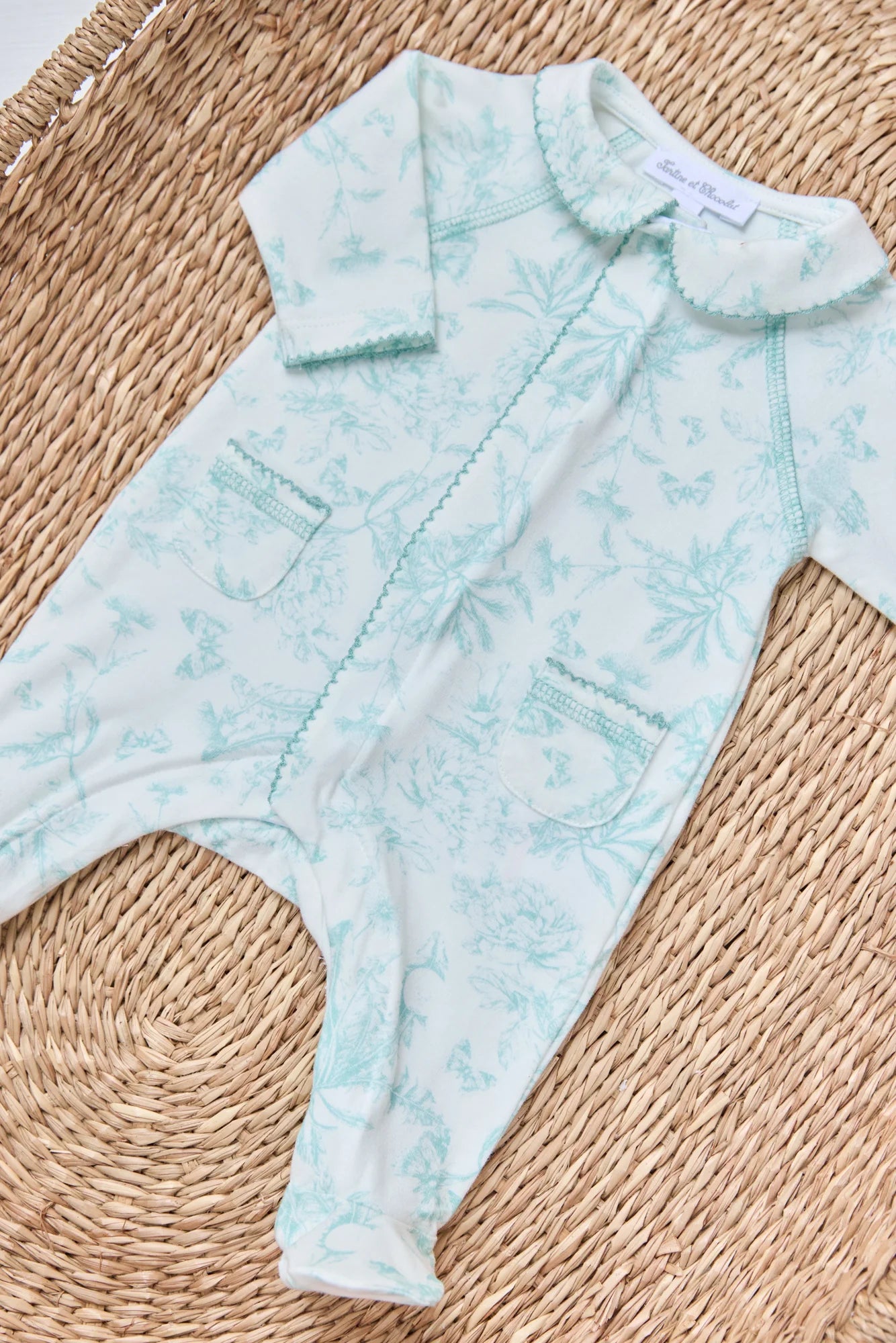 The Tartine et Chocolat Baby Girls' Printed Pajamas in light blue feature a floral Toile de Jouy pattern, Peter Pan collar, and front pockets, shown laid flat on a woven mat.