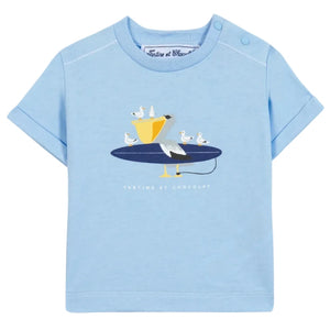 The Baby Boys’ and Boys’ Illustrated Cotton T-Shirt by Tartine et Chocolat features a light blue, 100% cotton fabric adorned with a playful graphic of a pelican and seagulls perched on a surfboard—an ideal choice for little explorers. The brand name “Tartine et Chocolat” is printed below the illustration.