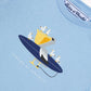 The Tartine et Chocolat Baby Boys’ and Boys’ Illustrated Cotton T-Shirt is a light blue top featuring a whimsical pelican riding a surfboard and carrying smaller birds in its beak, with “Tartine et Chocolat” printed below—a playful design made from 100% cotton, perfect for little explorers.