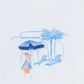 The Girls’ Beach Illustration T-Shirt by Tartine et Chocolat is a white cotton tee for girls, showcasing blue embroidery of a woman holding an umbrella, two lounge chairs, and a palm tree beneath the “Tartine et Chocolat” logo, with Santorini-inspired details for a charming seaside look.
