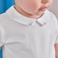 A toddler wearing the Tartine et Chocolat Baby Boys’ Pointed Collar Onesie in ecru with a delicately embroidered collar, gazing downward.