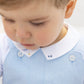 A close-up of a toddler wearing the Tartine et Chocolat Baby Boys’ Pointed Collar Onesie, featuring a light blue design with white buttons and an embroidered collar, looking downward.