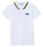 The Boys’ Surfer Polo Shirt by Tartine et Chocolat is a white polo featuring a blue and yellow striped collar and a small embroidered surfboard graphic on the left chest.