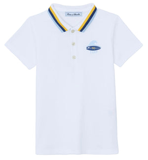 The Boys’ Surfer Polo Shirt by Tartine et Chocolat is a white polo featuring a blue and yellow striped collar and a small embroidered surfboard graphic on the left chest.