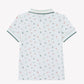 Tartine et Chocolat Baby Boys’ and Boys’ Knitted Polo Shirt, featuring short sleeves and a green collar with matching cuffs. This white cotton polo showcases an all-over print of dinosaurs, small red and green animals, and leafy accents for a playful look. Crafted from soft cotton for ultimate comfort. Back view shown.