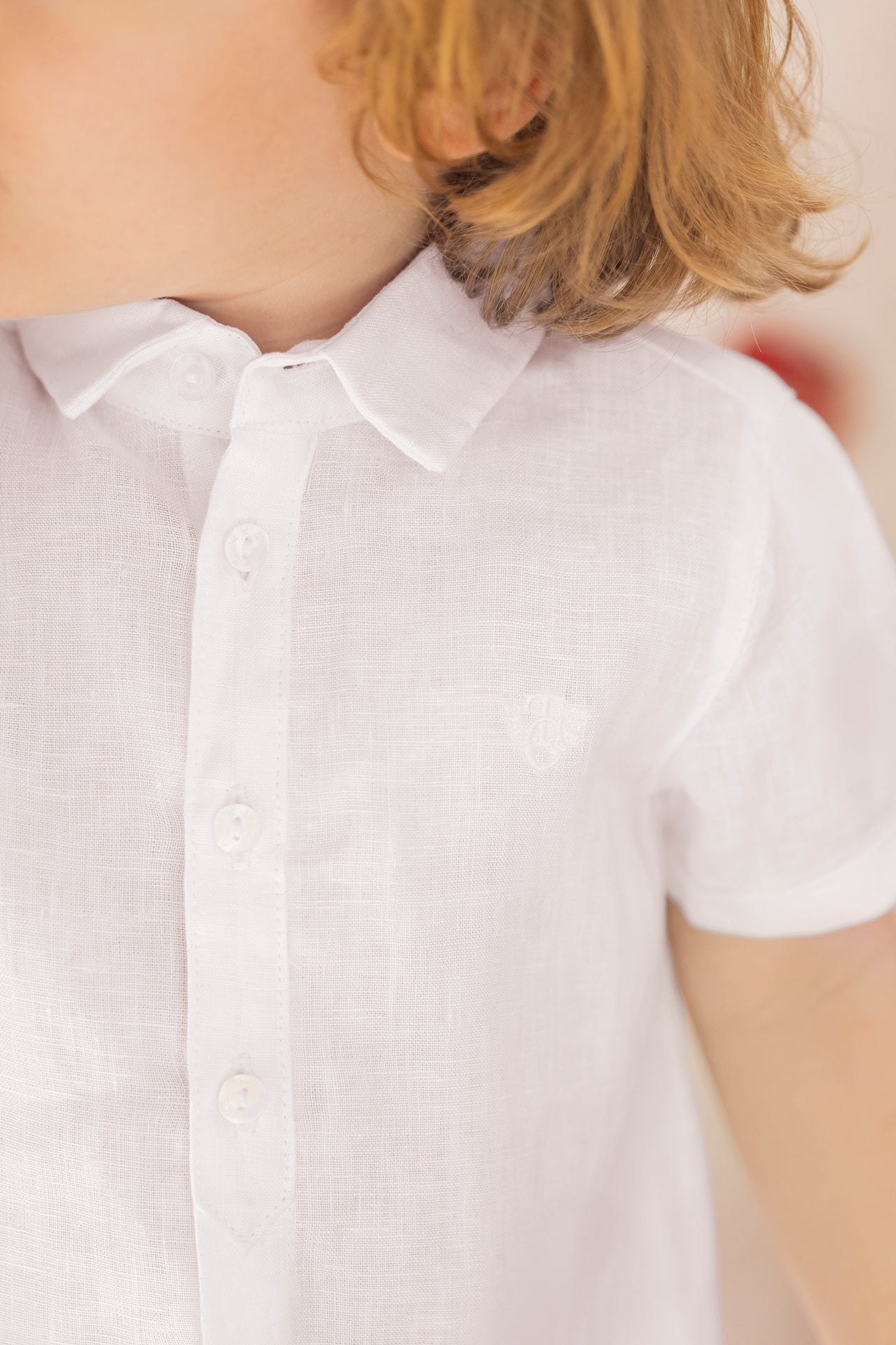 A child is seen from the shoulders to mid-torso wearing the Tartine et Chocolat Baby Boys’ and Boys’ Linen Collared Shirt in white—an elegant, short-sleeved option ideal for special occasions, with part of the face out of frame.