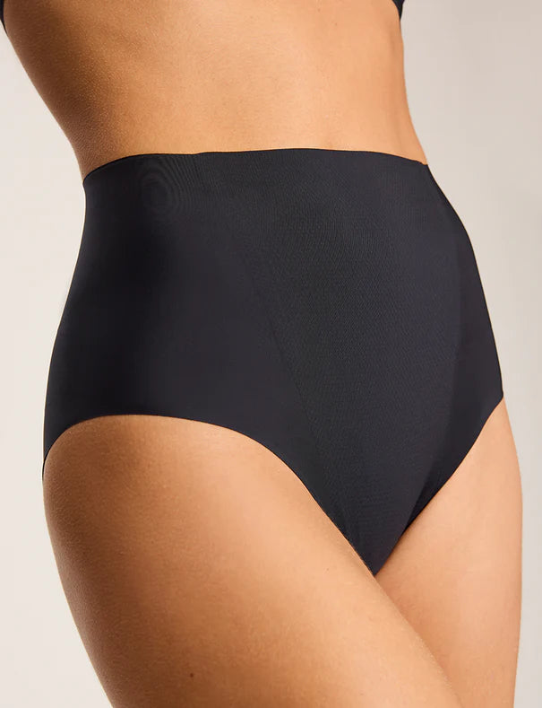 A person wears the Commando Zone Smoothing Brief—a high-rise, black shapewear brief with smoothing panels—shown from mid-torso to upper thigh against a neutral background.