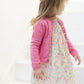 A young girl with light brown hair stands on white steps, looking to the side, wearing a pink Tartine et Chocolat Baby Girls’ and Girls’ Openwork Cardigan over a floral dress.