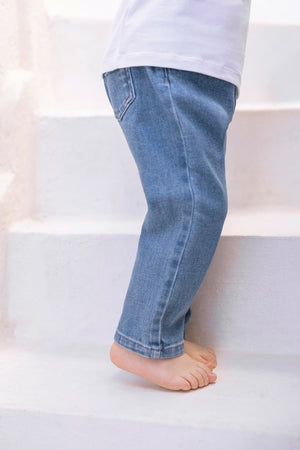 A little explorer wearing Tartine et Chocolat Baby Boys’ and Boys’ John Blue Jeans is walking up white stairs barefoot, paired with a crisp white shirt.
