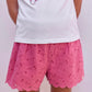 A child stands facing away against a plain light background, dressed in Tartine et Chocolat Baby Girls’ and Girls’ English Embroidery Shorts—white shorts featuring delicate embroidery and a scalloped hem—paired with a simple white T-shirt.