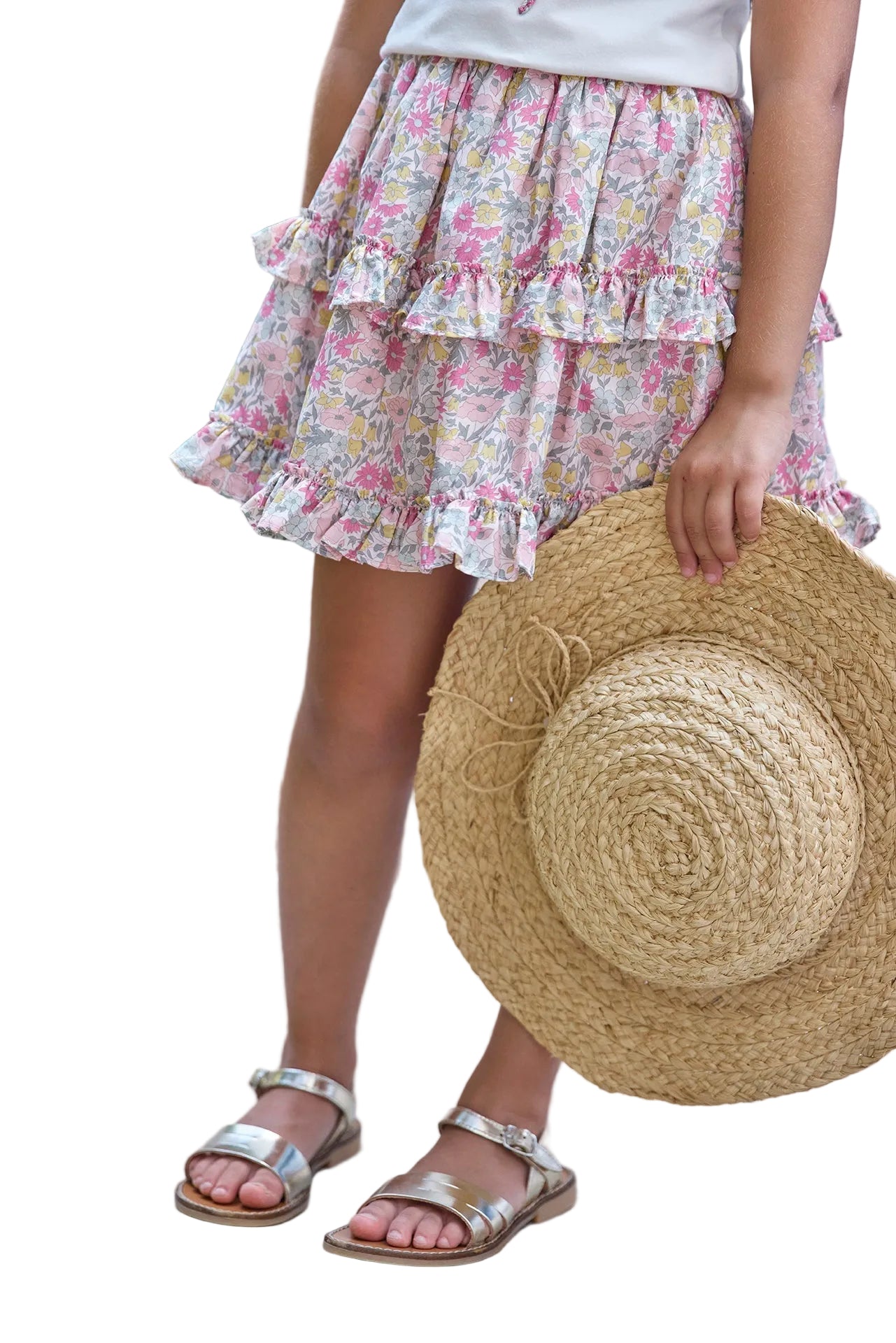 A child wearing the Tartine et Chocolat Girls’ Liberty Fabric Print Skirt and silver sandals holds a large straw hat, standing against a white background.