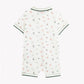 The Tartine et Chocolat Baby Boys’ Short Jumpsuit showcases a charming white design adorned with playful green and orange dinosaur prints. It features short sleeves and soft green trim accenting the collar, sleeves, and leg openings. Crafted for comfort, this jumpsuit is presented on a plain white background.