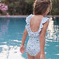 A young girl with braided hair stands at the edge of a swimming pool, facing away from the camera, wearing the Tartine et Chocolat Girls’ Liberty Fabric Print Swimsuit.