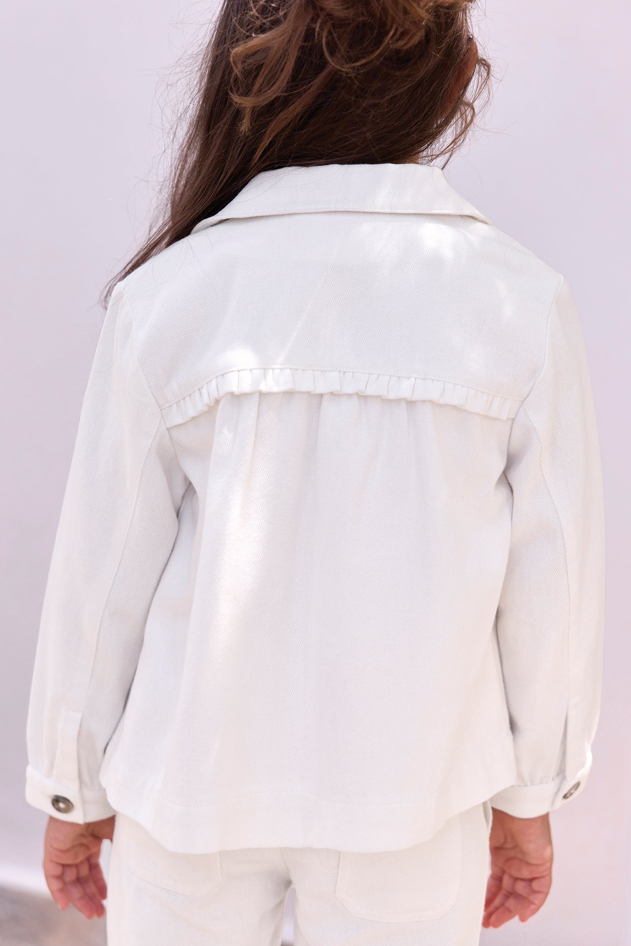 A child with long brown hair is shown from behind, wearing the Tartine et Chocolat Girls’ Cotton Jacket with embroidered pockets and matching pants, set against a plain light background.