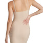 A woman is shown from the back wearing the Commando Zone Smoothing Full Slip, a beige, fitted dress with adjustable straps. Her right hand rests on her hip.