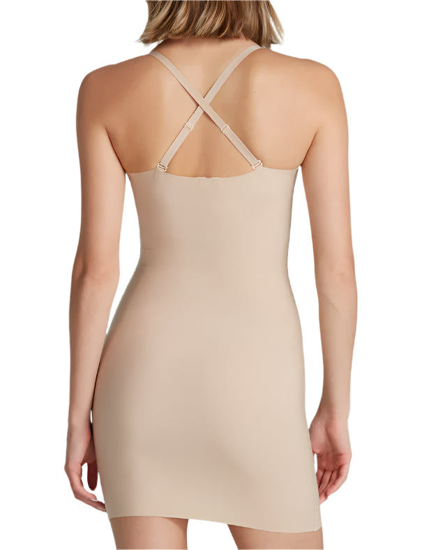 A woman is seen from the back wearing the Commando Zone Smoothing Full Slip, a beige, form-fitting dress with adjustable crisscross straps.