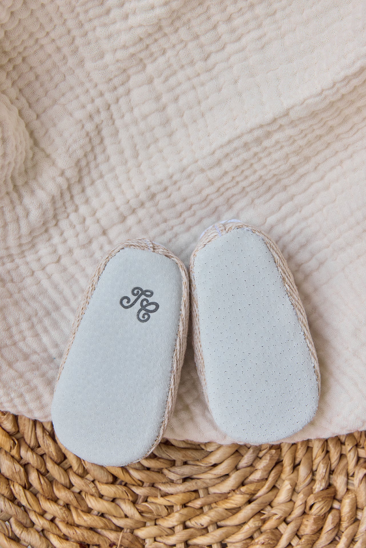 A pair of Tartine et Chocolat Baby Girls’ Liberty Fabric Espadrille Slippers with textured white soles rest on a cream-colored blanket and woven mat.