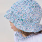A young child is seen in profile against a light background, wearing a white shirt and the Tartine et Chocolat Baby Girls’ Country Club Hat—a cotton summer hat with a floral pattern.