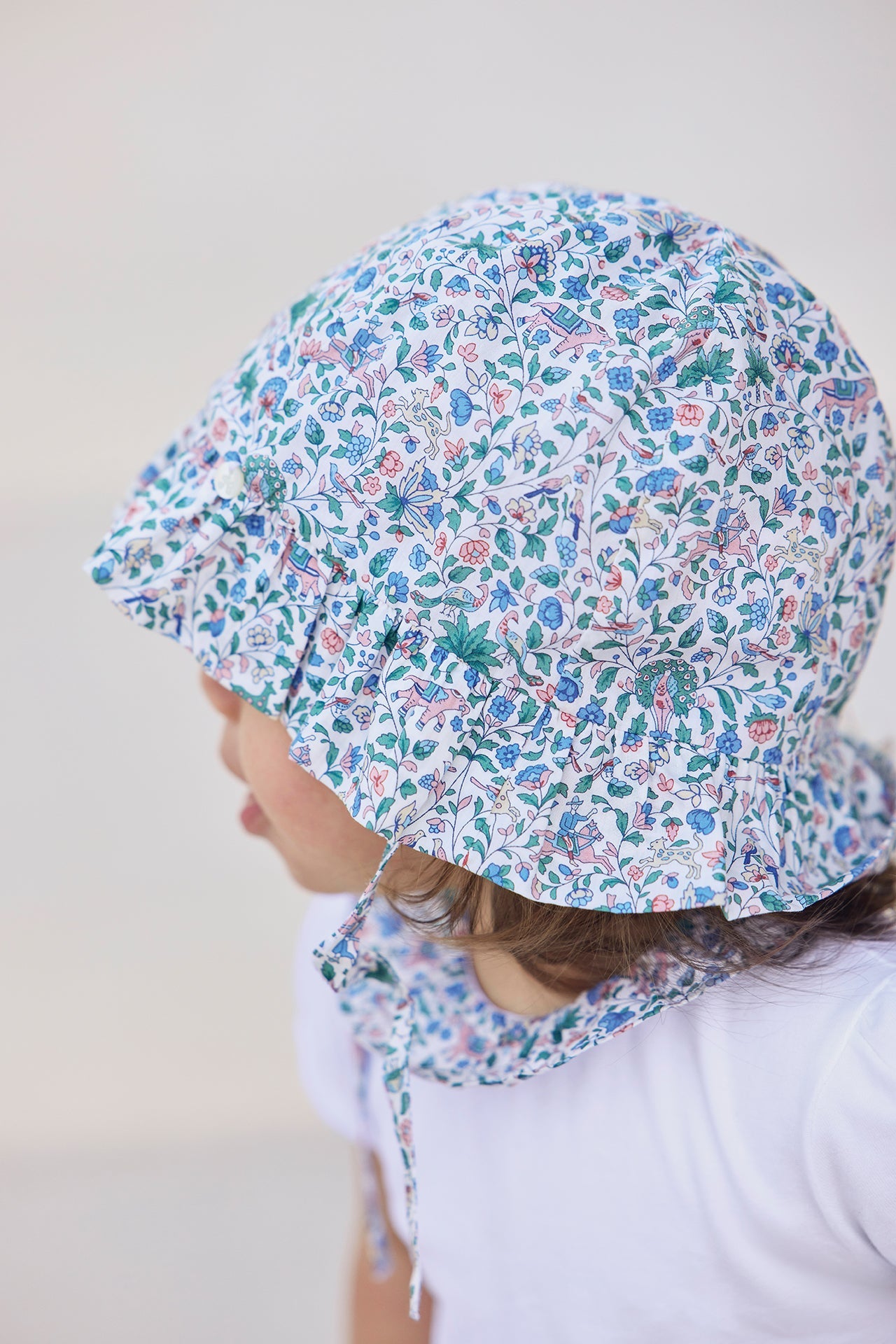 A young child is seen in profile against a light background, wearing a white shirt and the Tartine et Chocolat Baby Girls’ Country Club Hat—a cotton summer hat with a floral pattern.