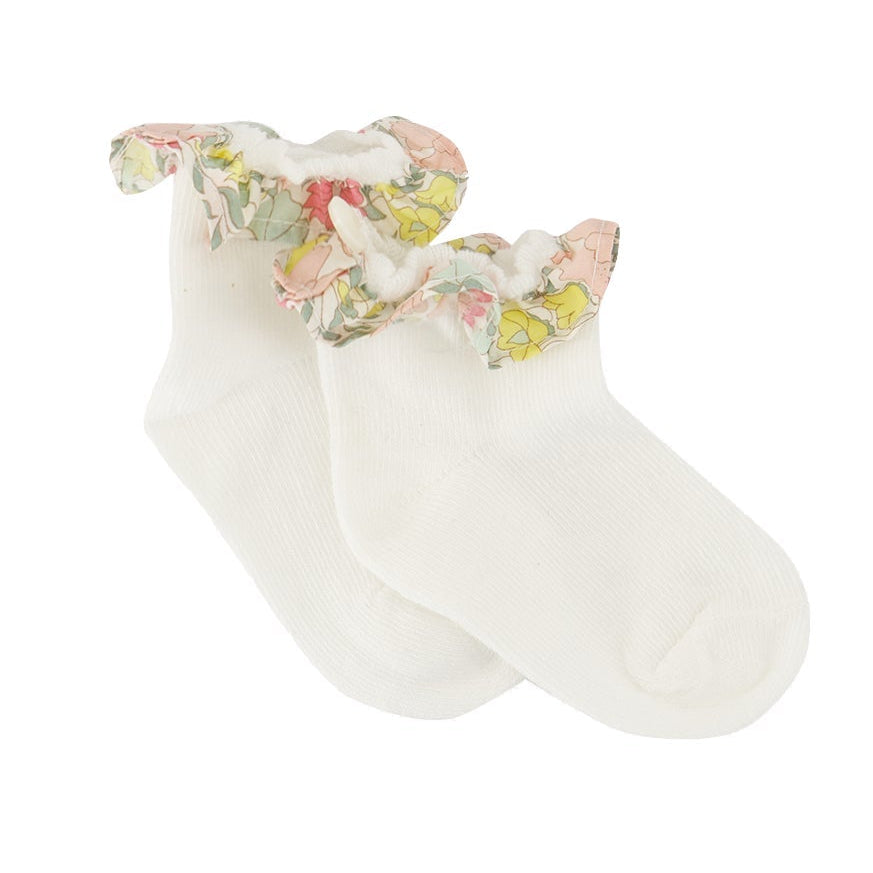 A pair of Tartine et Chocolat Baby Liberty Print Socks in white cotton, featuring a delicate floral ruffled trim around the ankle, displayed on a plain white background. These charming socks add a touch of sweetness to any little one’s outfit.