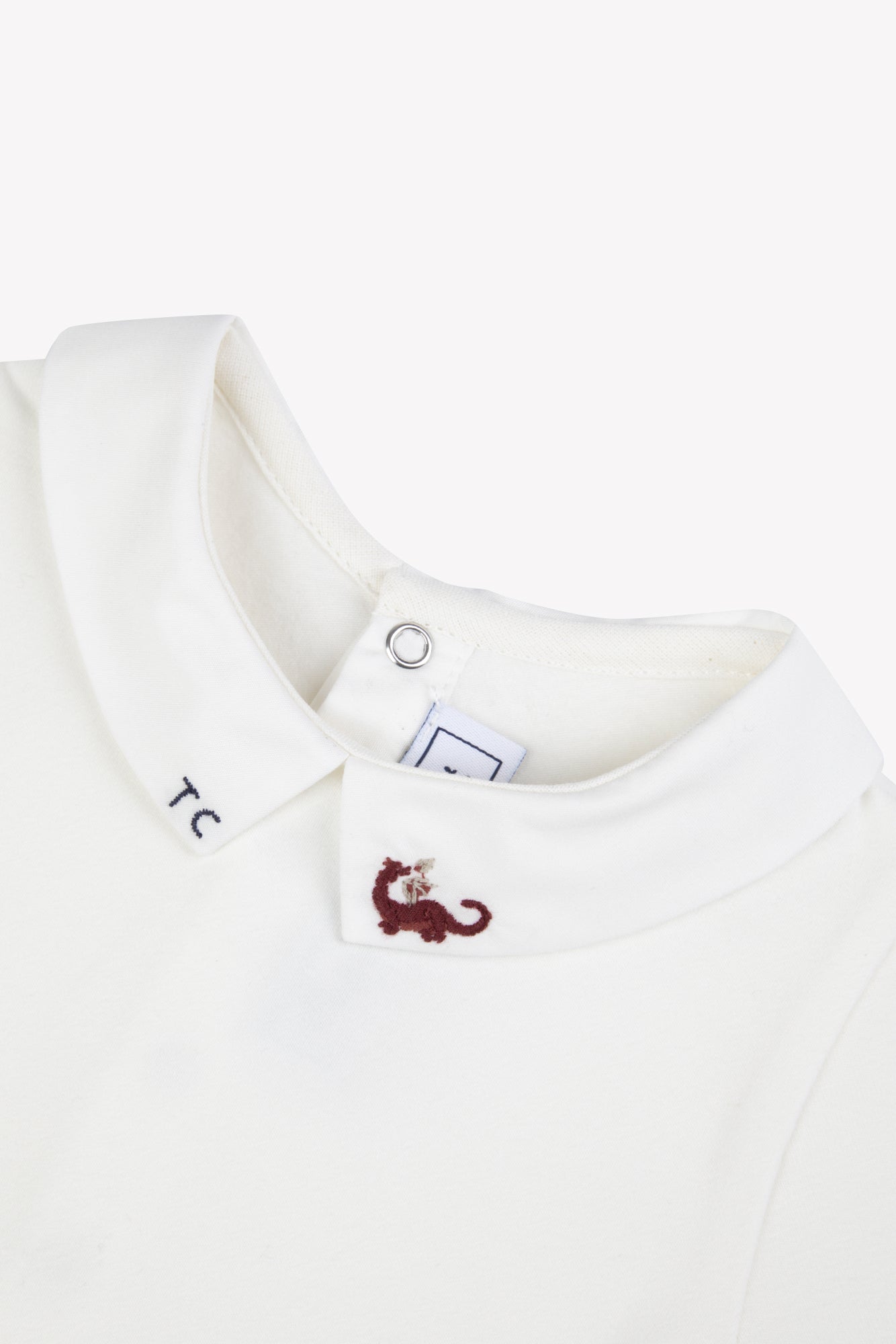 Close-up of the Tartine et Chocolat Baby Boys’ Dinosaur Bodysuit, featuring a white collar with “TC” embroidered on one tip and a playful red cat motif on the other, echoing the charming details often seen in high-quality baby rompers.