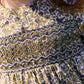 Close-up of a child wearing the Tartine et Chocolat Girls’ Liberty Embroidery Round Neck Cotton Dress in olive cotton, featuring intricate smocking across the chest and delicate Liberty floral embroidery; partial view of face and brown hair evokes the charm of an English garden.