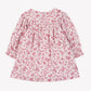 The Girls’ Floral Print Cotton Dress by Tartine et Chocolat is a pink, long-sleeve dress for children, made from soft unbleached cotton. It features a floral print, round neckline, ruffled cuffs, and a back zipper closure. The dress is displayed against a plain white background.