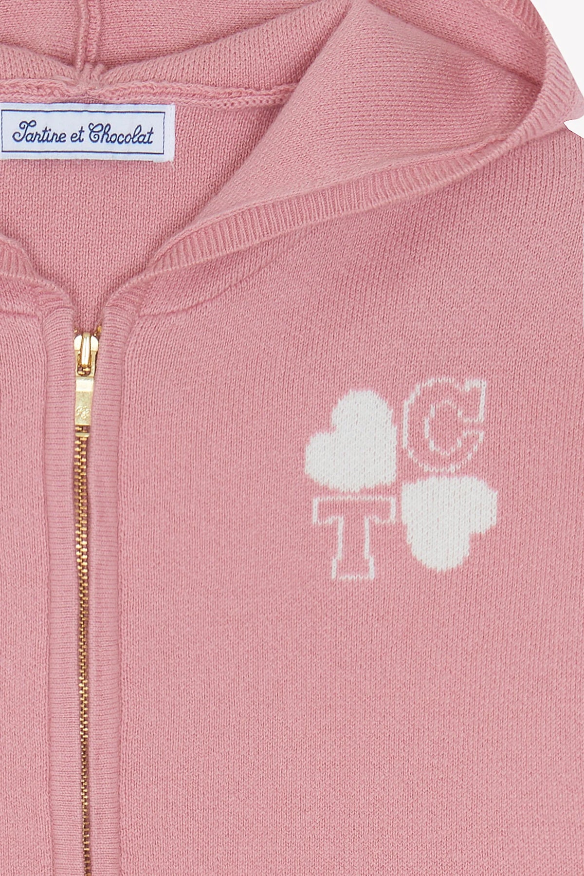Close-up of the Girls’ Wool Hood Cotton Jogging Suit by Tartine et Chocolat, featuring a pink zip-up hoodie with a gold zipper, white “TC” and heart shapes on the chest, and a “Tartine et Chocolat” label at the neck. This charming piece is part of the Paris Mon Amour kids tracksuit collection, crafted from soft cotton and wool for comfort and style.