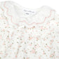 Introducing the Baby Girls’ Ruffle Collar Pajama by Tartine et Chocolat—a charming white baby pajama featuring a ruffled collar, scalloped lace trim, and delicate pink floral print. Expertly crafted with the same attention to detail as Tartine et Chocolat’s signature pajamas for girls, this elegant piece captures the timeless appeal of classic baby sleepwear. The label reads “Tartine et Chocolat.”.