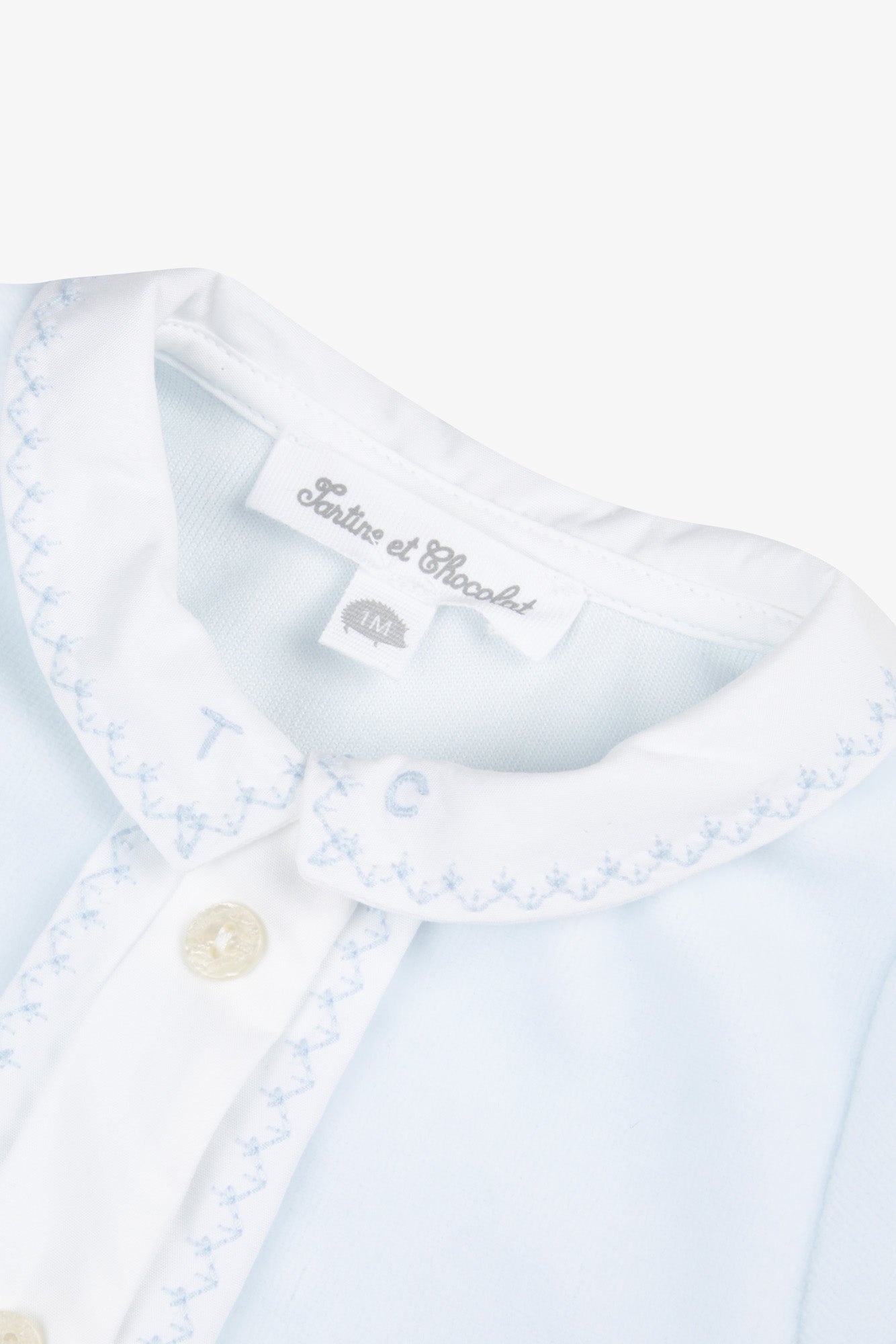 Close-up of the Baby Boys’ Velvet Pointed Collar Pajamas in light blue by Tartine et Chocolat, featuring a white collar delicately embroidered with the letters “T” and “C,” blue stitching, and buttons. This charming piece captures the timeless elegance of pointed collar pajamas, making it an exceptional choice for baby boys’ sleepwear.
