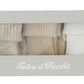 A rectangular box labeled “Tartine et Chocolat” in white script displays the Cotton Sock Set, featuring three pairs of ribbed toddler socks in gray, beige, and white. Made from gentle materials suitable for sensitive baby skin, the set is visible through a clear window on the box.
